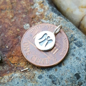 Pu&ograve; includere: Un piccolo ciondolo rotondo in argento con un design a angelo ritagliato. Il ciondolo &egrave; mostrato su un centesimo come riferimento delle dimensioni. L'angelo ha le ali spiegate e una forma semplice ed elegante. Il ciondolo ha un piccolo anello per una catena.