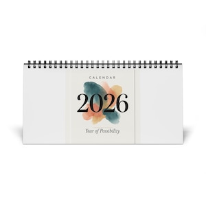 Puede incluir: Un calendario de escritorio blanco para el año 2026, con encuadernación en espiral negra. El calendario presenta la palabra "CALENDAR" en la parte superior, el número "2026" en fuente negra grande y las palabras "Year of Possibility" debajo.