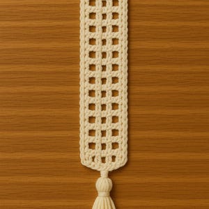 Puede incluir: Marcapáginas de ganchillo hecho a mano de color crema, con un patrón de rejilla y una borla. El marcapáginas rectangular presenta una serie de cuadrados abiertos, creando un efecto de enrejado. La borla está unida en la parte inferior.