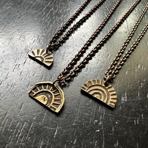 Puede incluir: Tres collares de oro con un colgante de medio sol. Cada collar tiene una cadena de diferente longitud.