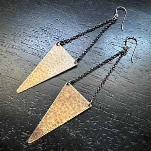 May include: A pair of triangle-shaped earrings with a hammered texture and black chain links. The earrings are made of brass and have a rustic, industrial look.