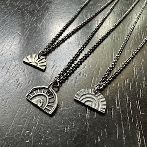 Puede incluir: Tres collares de plata con un colgante de medio círculo que presenta un diseño de sol estilizado. Cada colgante tiene un patrón diferente de líneas y curvas.