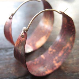 May include: A pair of copper hoop earrings with a hammered finish. The earrings are a warm, reddish-brown color and have a slightly irregular shape.