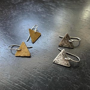 May include: A pair of triangle-shaped earrings with hammered metal finishes. One earring is silver and the other is gold.