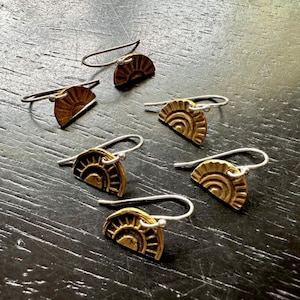 Puede incluir: Un conjunto de seis pendientes de color dorado con un diseño de medio sol. Cada pendiente tiene una pequeña perla redonda de plata en la parte superior del gancho.