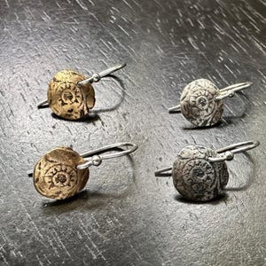 May include: Four pairs of silver and gold earrings with a circular design. The earrings are made of metal and have a simple, elegant style.