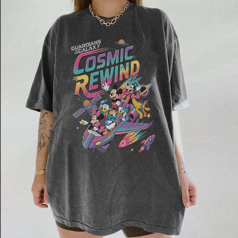 Puede incluir: Una camiseta de manga corta gris carb&oacute;n con un estampado gr&aacute;fico colorido de personajes de Disney en una nave espacial. El texto dice Guardians of the Galaxy Cosmic Rewind. El dise&ntilde;o incluye a Mickey, Minnie, Donald, Daisy, Goofy y Pluto.