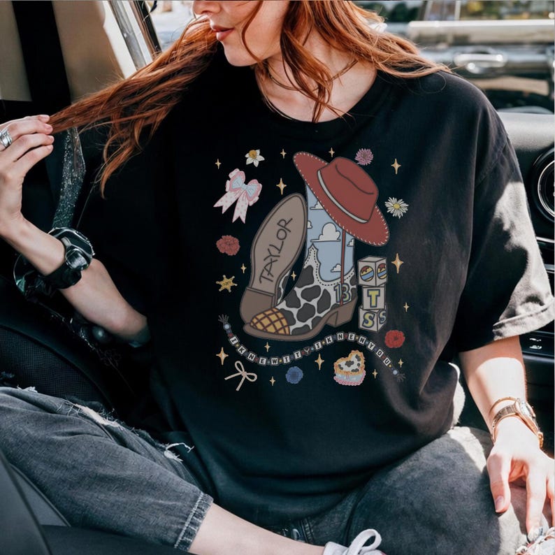 May include: A black t-shirt featuring a graphic print of a cowboy boot with a cow print pattern, a red hat, the name Taylor, the number 13, stacked blocks with letters, a bow, flowers, and a beaded string with the text I KNEW YOU WERE TROUBLE.