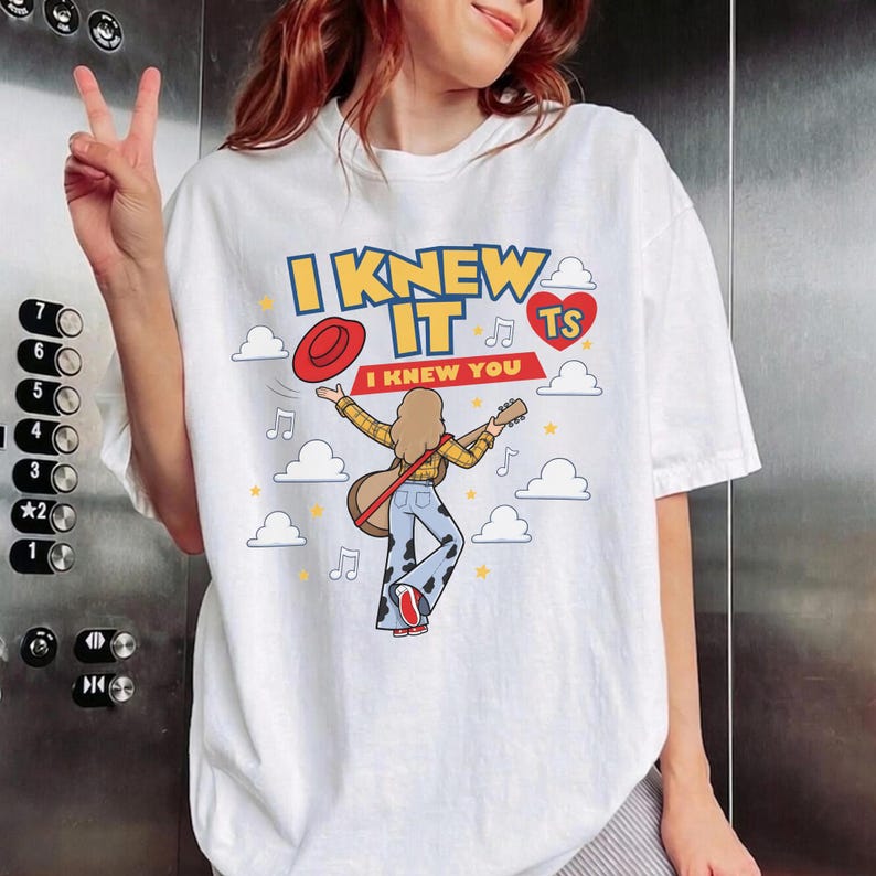 K&ouml;nnte beinhalten: Ein wei&szlig;es Kurzarm-T-Shirt mit einer Grafik einer Person mit langen Haaren, die Gitarre spielt, ein gelbes kariertes Hemd und eine Hose mit Kuhflecken tr&auml;gt. Der Text lautet I KNEW IT I KNEW YOU, erg&auml;nzt durch ein rotes Herz und einen roten Hut.
