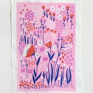 May include: A pink tea towel with a floral pattern featuring red, white, and blue flowers. The text "Linda Fryer" is printed in the bottom right corner.