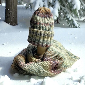 May include: A knitted hat and scarf set in a winter scene. The hat and scarf are made of a multicolored yarn with shades of beige, brown, red, and green. The hat has a folded brim. The scarf is wrapped around the neck.