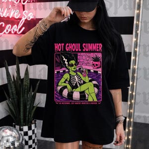May include: Black t-shirt with the text "HOT GHOUL SUMMER" and a graphic of a green monster in a pool float. The shirt also has the text "NO MELTDOWNS, JUST MAKEUP, MONSTERS & MAYHEM".