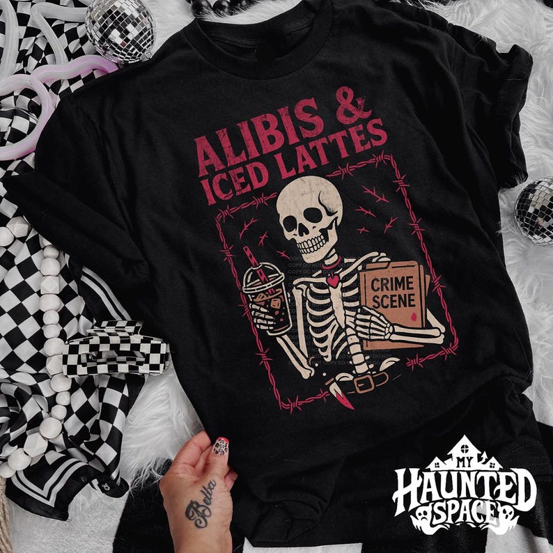 May include: Black t-shirt with a skeleton graphic holding a coffee and a "Crime Scene" file. The text "ALIBIS & ICED LATTES" is above the skeleton. The design is framed by a barbed wire border.