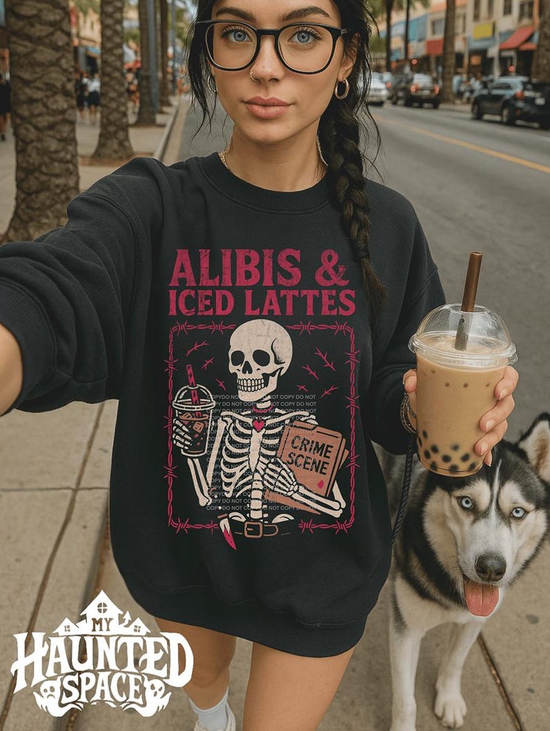 May include: Black sweatshirt with the text "ALIBIS & ICED LATTES" and a skeleton graphic holding a drink and a book labeled "CRIME SCENE". A husky dog with blue eyes is next to the person wearing the sweatshirt.