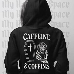 May include: Black hoodie with the text "CAFFEINE & COFFINS" in white. The design includes a coffin with a cross and a skeleton hand holding a drink with ice cubes. The hoodie has a hood.
