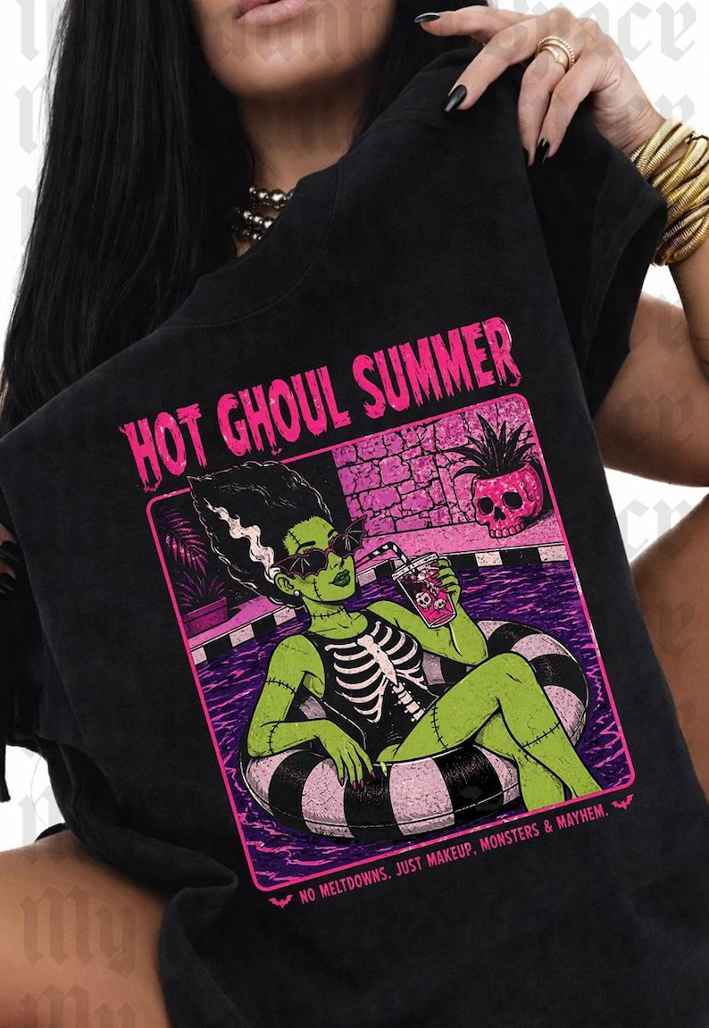 May include: Black t-shirt with a graphic of a green monster in a pool floatie, with the text "HOT GHOUL SUMMER". The monster is wearing sunglasses and a skeleton costume. The image includes the text "NO MELTDOWNS. JUST MAKEUP. MONSTERS & MAYHEM."