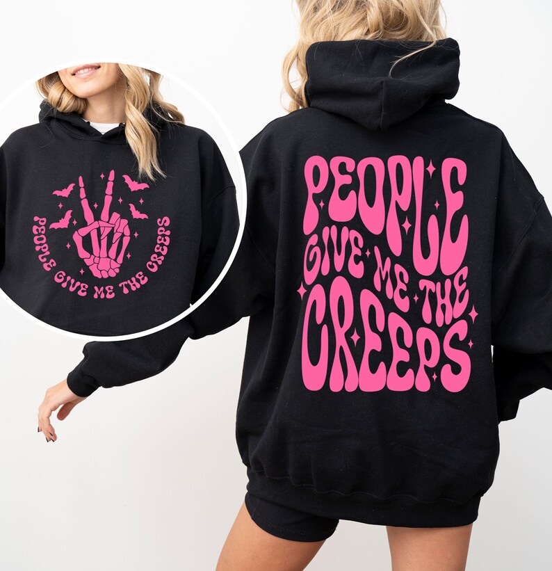 K&ouml;nnte beinhalten: Schwarzer Kapuzenpullover mit einem pinkfarbenen Aufdruck auf der R&uuml;ckseite, der in einer Retro-Schrift "People Give Me The Creeps" lautet. Die Vorderseite des Pullovers hat einen pinkfarbenen Aufdruck einer Skeletthand, die ein Peace-Zeichen macht, mit Flederm&auml;usen, die um sie herum fliegen, und dem Text "People Give Me The Creeps".