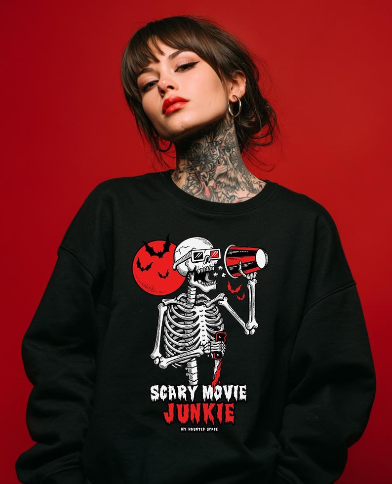 May include: Black sweatshirt featuring a skeleton with 3D glasses holding a megaphone and a red cup. A red moon with bats is behind the skeleton. The text "SCARY MOVIE JUNKIE" is printed below the skeleton.