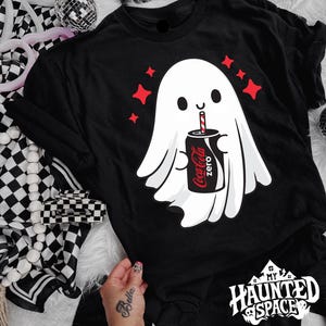 May include: Black t-shirt with a white ghost graphic drinking from a Coca-Cola Zero can. Red star shapes are above the ghost. The text "My Haunted Space" is at the bottom. A Halloween-themed design.