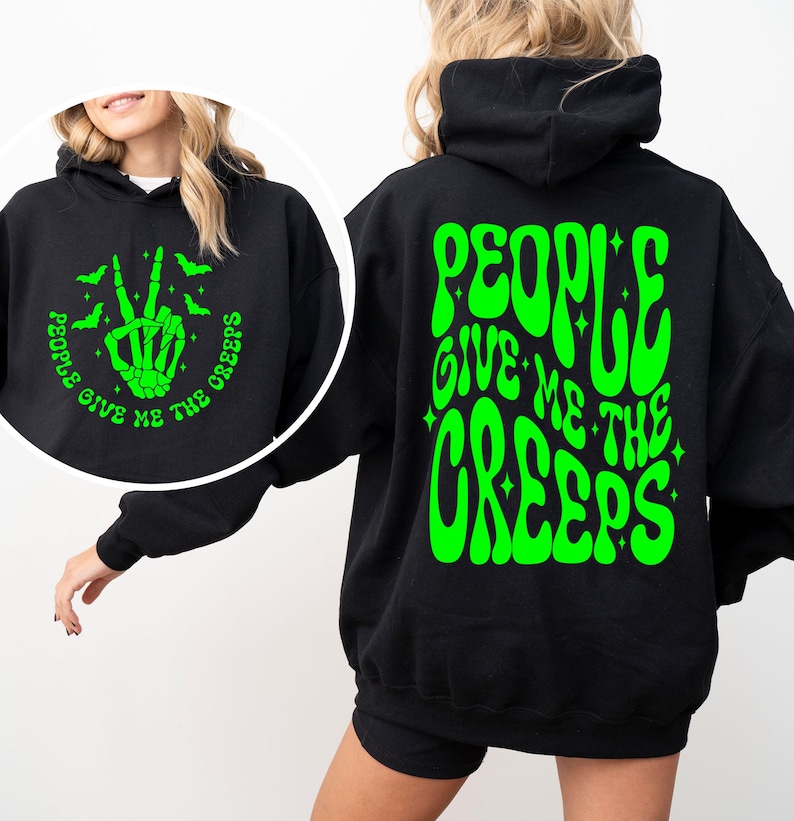 K&ouml;nnte beinhalten: Schwarzer Hoodie mit einem gr&uuml;nen Aufdruck auf der R&uuml;ckseite, der in einer Retro-Schrift "People Give Me The Creeps" lautet. Die Vorderseite des Hoodies zeigt ein gr&uuml;nes Motiv einer Skeletthand, die ein Peace-Zeichen macht, mit Flederm&auml;usen, die um sie herum fliegen. Der Text um die Hand herum lautet "People Give Me The Creeps".