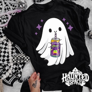 May include: Black t-shirt featuring a cartoon ghost holding a can of "Witch's Brew Alan" with a purple and green design. The shirt has the text "My Haunted Space" in white. Purple stars are scattered around the ghost.