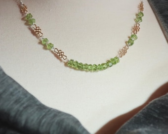 May include: A delicate necklace featuring a strand of small, faceted, light green gemstones. The necklace has silver-colored chain and decorative gold-colored filigree accents. The necklace is displayed on a mannequin.