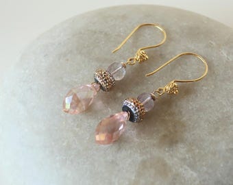 May include: A pair of gold-tone drop earrings featuring faceted peach-colored teardrop beads, small clear round beads, and textured metallic spacers. The earrings are suspended from gold-tone curved ear wires with small decorative accents.
