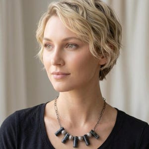 May include: A necklace featuring a dark metal chain with alternating cylindrical black speckled beads and small, round, textured silver-toned beads. The pendant section consists of five black cylindrical beads separated by four silver-toned beads.