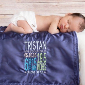 May include: A blue satin baby blanket with white trim and embroidered text. The text reads "TRISTAN MILLS VAIOIO 05.10.16 6 lb 15 oz 19.5 inches 3:08 PM".