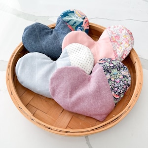 Peut inclure: Un assortiment d'articles en tissu en forme de c&oelig;ur dans un panier tress&eacute;. Les c&oelig;urs sont faits de divers tissus, notamment du denim, des imprim&eacute;s floraux et des couleurs unies comme le rose et le lavande. Le panier est en mat&eacute;riau tiss&eacute; brun clair.
