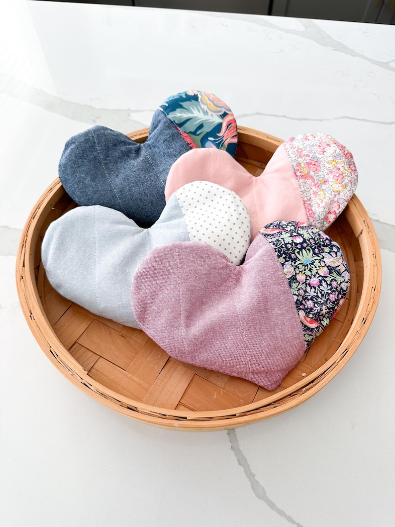 Peut inclure: Un assortiment d'articles en tissu en forme de c&oelig;ur dans un panier tress&eacute;. Les c&oelig;urs sont faits de divers tissus, notamment du denim, des imprim&eacute;s floraux et des couleurs unies comme le rose et le lavande. Le panier est en mat&eacute;riau tiss&eacute; brun clair.