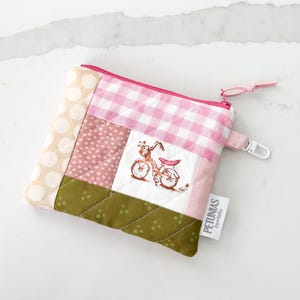 Op de afbeelding: Een patchwork etui met ritssluiting met een roze ruitpatroon, stippen en een fietsborduurwerk. De etui heeft een roze rits en een klein wit label met "PETUNIAS by kelly".