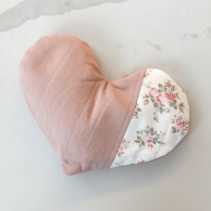Peut inclure: Un oreiller en forme de c&oelig;ur avec un dessus matelass&eacute; rose poudr&eacute; et un fond &agrave; motifs floraux. Le motif floral pr&eacute;sente des roses roses et rouges sur un fond blanc. L'oreiller est con&ccedil;u pour le confort et la d&eacute;tente.