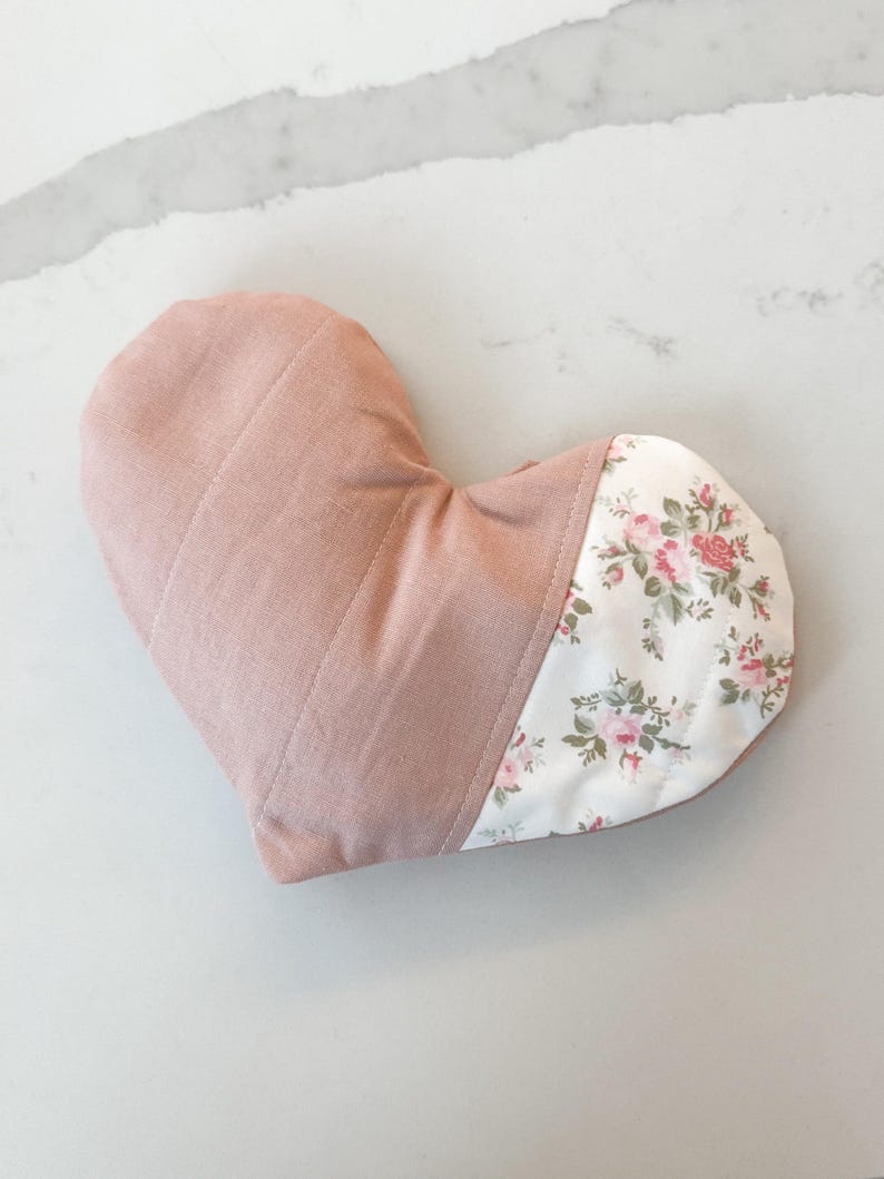 Peut inclure: Un oreiller en forme de c&oelig;ur avec un dessus matelass&eacute; rose poudr&eacute; et un fond &agrave; motifs floraux. Le motif floral pr&eacute;sente des roses roses et rouges sur un fond blanc. L'oreiller est con&ccedil;u pour le confort et la d&eacute;tente.