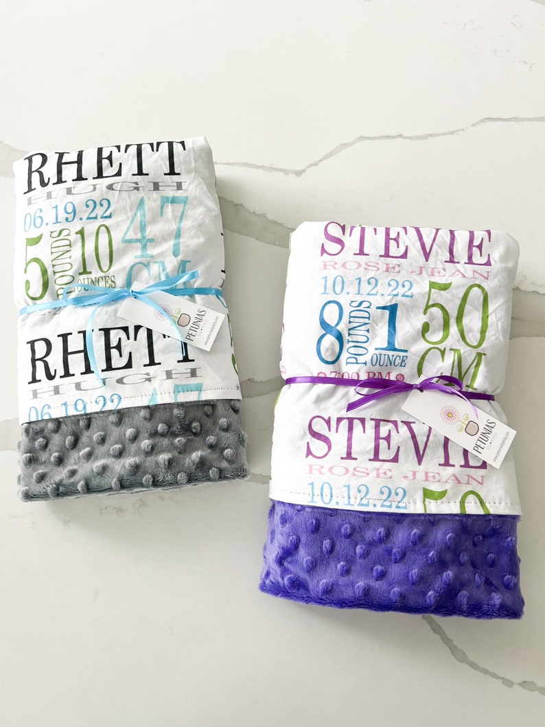 Puede incluir: Dos mantas de beb&eacute; personalizadas con tejido minky gris y morado. Las mantas presentan un tejido blanco con texto colorido, incluyendo nombres, fechas de nacimiento, pesos y longitudes. El texto en la manta gris dice: "Rhett Hugh 06.19.22 5 libras 10 onzas 47 cm". El texto en la manta morada dice: "Stevie Rose Jean 10.12.22 8 libras 1 onza 50 cm".