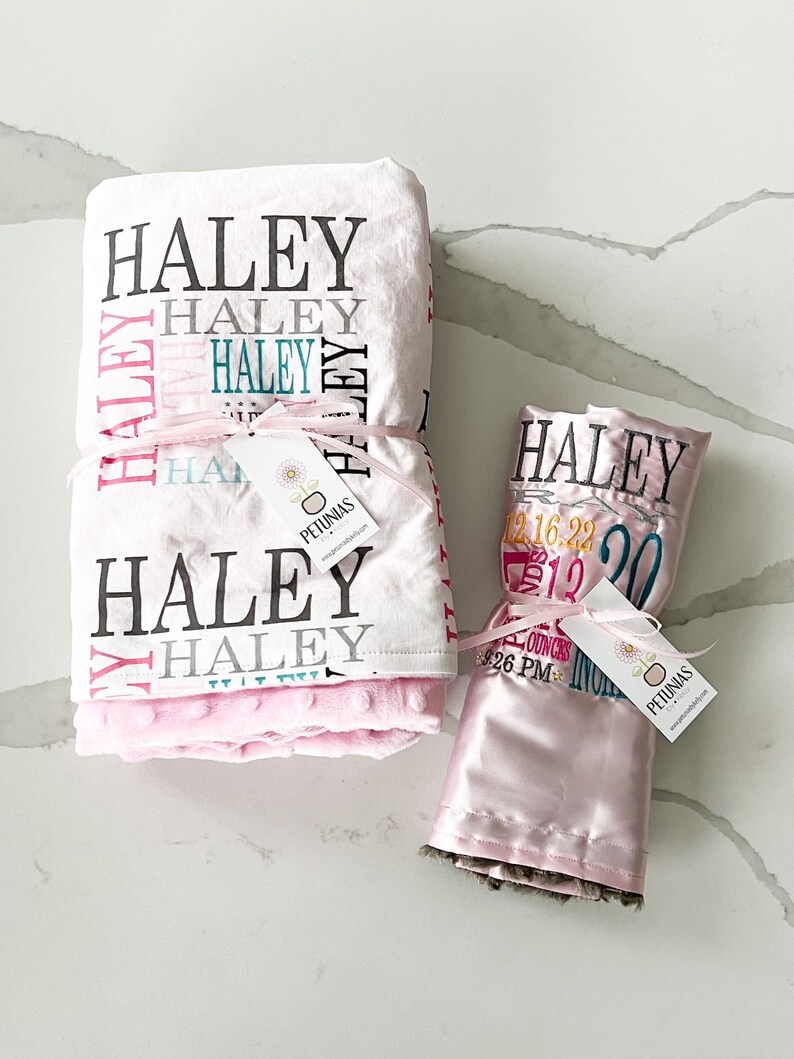 Puede incluir: Dos mantas de beb&eacute; rosas con el nombre "Haley" bordado. Una manta es blanca con lunares rosas y la otra es de sat&eacute;n con ribete de piel marr&oacute;n. Ambas mantas tienen una etiqueta con el nombre "Petunias" en ellas.