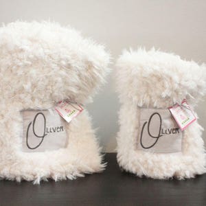 May include: Two white fluffy blankets with the name "Oliver" embroidered on them. The blankets are folded and have a tag attached.