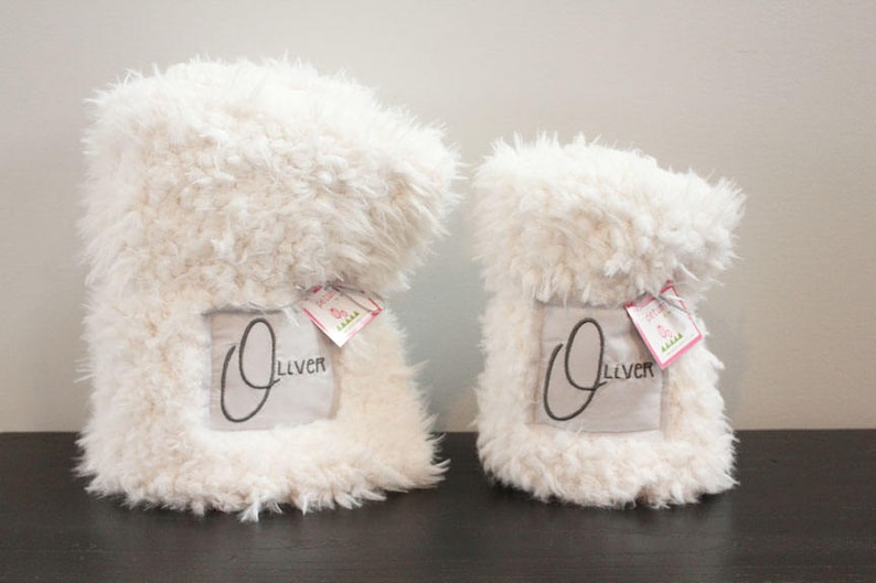 May include: Two white fluffy blankets with the name "Oliver" embroidered on them. The blankets are folded and have a tag attached.