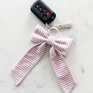 May include: A key fob with a black remote and a Toyota Sienna key, attached to a silver keyring with a mauve and white striped bow. The bow is made of fabric and has long, flowing tails.