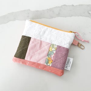 Op de afbeelding: Een klein roze en groen patchwork etui met een witte kanten rand en een gele rits. Het etui heeft een witte stippenrand en een label met de tekst "PETUNIAS by KELLY".
