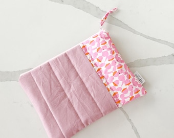 May include: A pink quilted zippered pouch with a white fabric lining featuring a pink and orange bird print. The pouch has a pink zipper pull and a white label that reads "PetitBous."