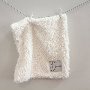 May include: A white fluffy blanket with a small white tag that says "Oliver" on it.