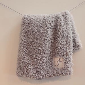 May include: A grey fluffy blanket with a white label that says "Jack" on it.