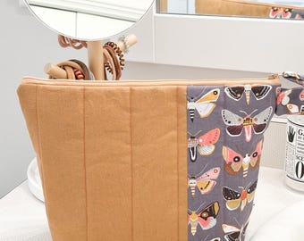 May include: A quilted brown zippered pouch with a gray fabric panel featuring a repeating pattern of colorful butterflies.