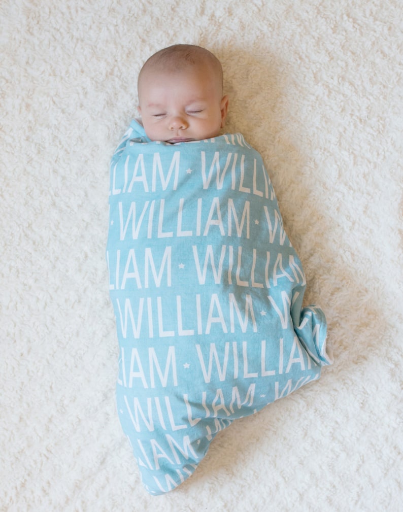 Puede incluir: Un beb&eacute; envuelto en una manta de muselina azul claro con el nombre "William" impreso en blanco repetidamente.