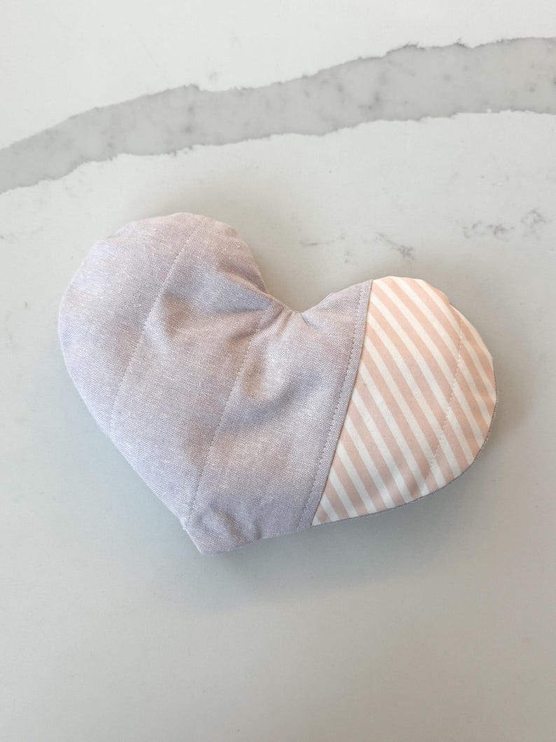 Peut inclure: Un gant de cuisine en forme de c&oelig;ur, matelass&eacute;. Il est principalement de couleur lavande clair avec des coutures verticales. Une section pr&eacute;sente un motif &agrave; rayures blanches et roses claires.