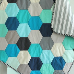 May include: A blue, green, gray, and white hexagonal patterned quilt with a white and gray striped backing.