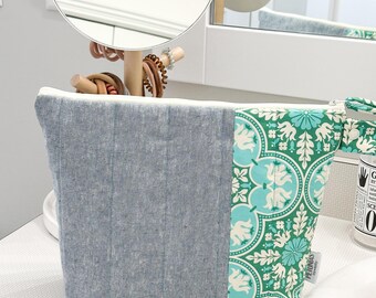 May include: A blue and green quilted zippered pouch with a floral pattern. The pouch is sitting on a white countertop.