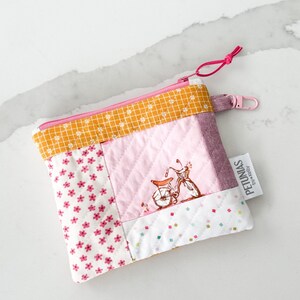 Op de afbeelding: Een roze en gele patchwork-ritszakje met een klein fietsontwerp en de tekst "PETUNIAS by Regina" aan de zijkant.