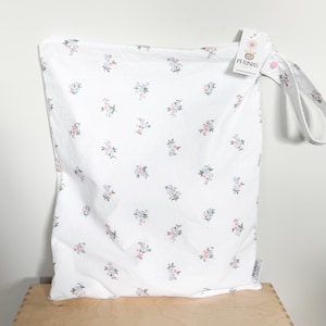 May include: White cloth bag with a floral pattern of pink and blue flowers. The bag has a handle and a tag that reads "PETUNIAS". The bag is sitting on a wooden surface.